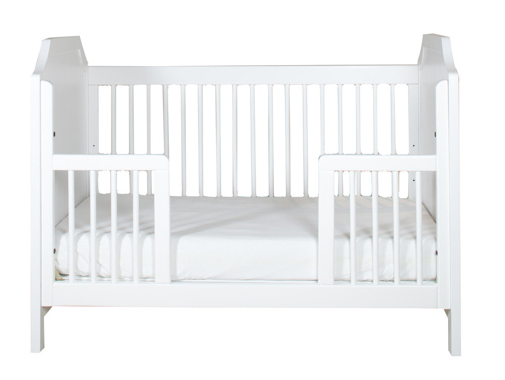 A white toddler guardrail with a crib, designed to allow toddlers to crawl in and out safely.