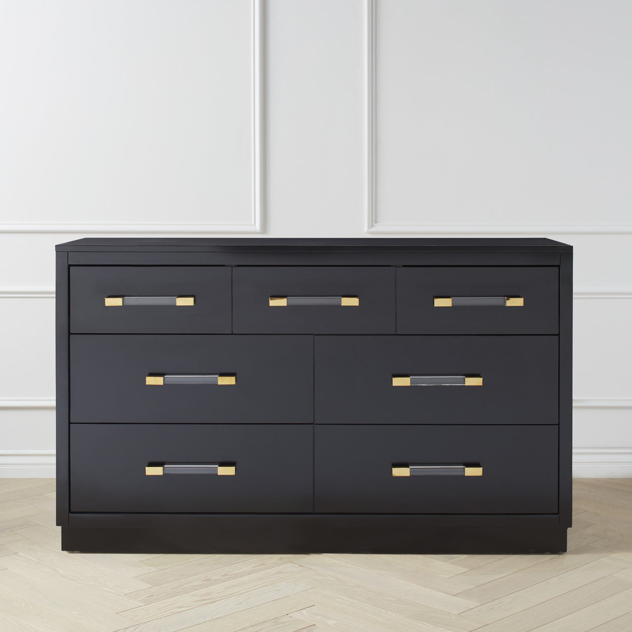 A black dresser with multiple drawers, featuring gold-colored knobs on the drawers and a brass or nickel finish on the drawer handles.